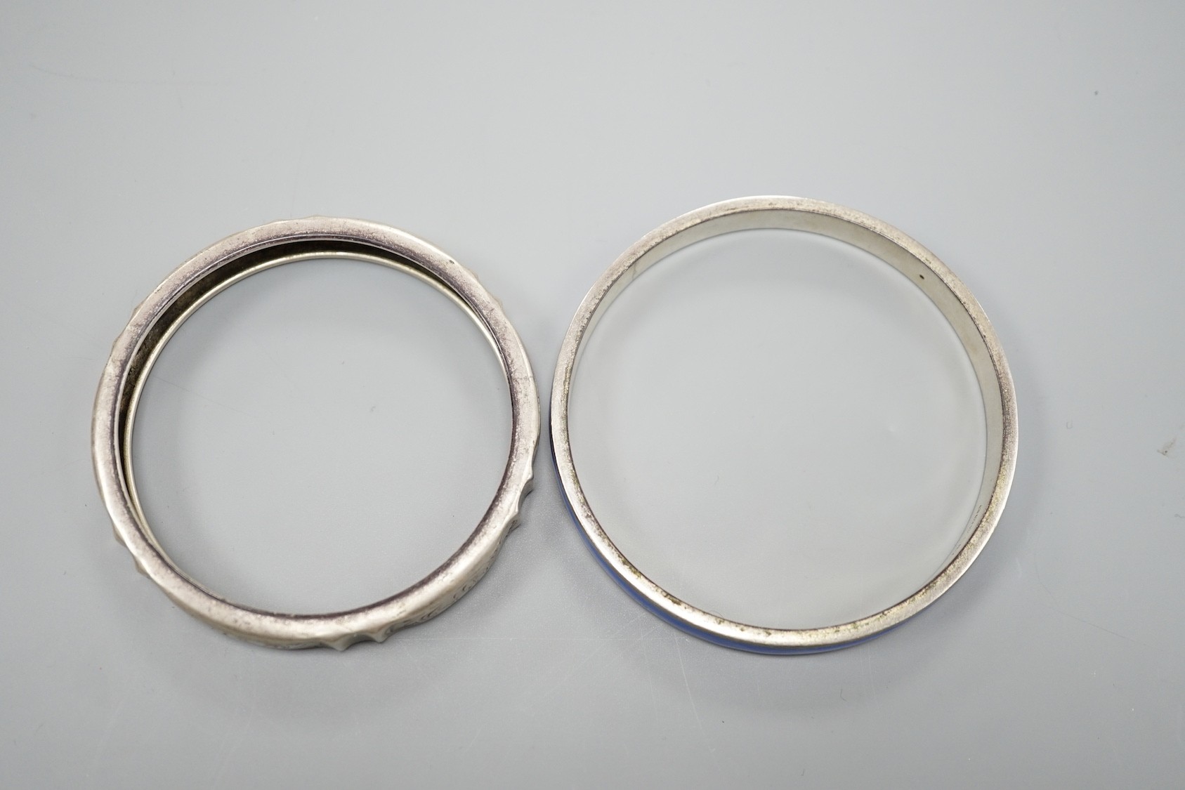 A 1920's silver and blue enamel bangle and an engraved white metal bangle.